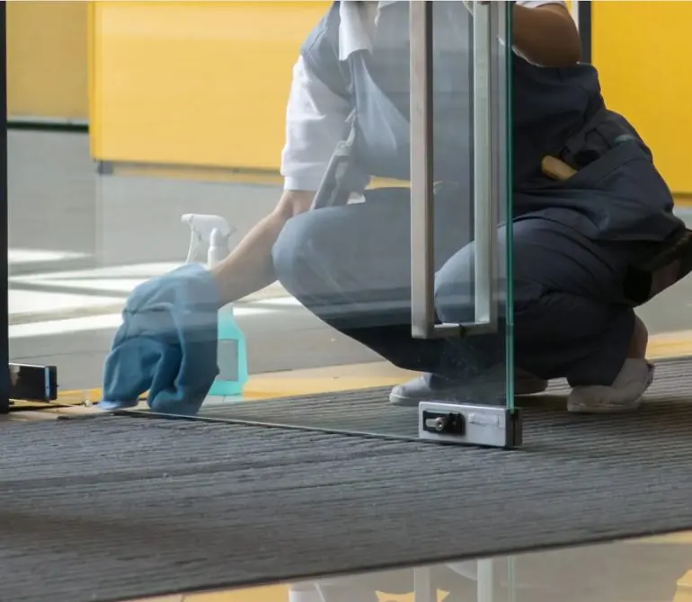 Empleado agencia de limpieza limpiando puerta vidriada